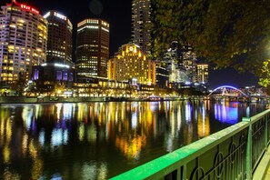 A nighttime cityscape with illuminated buildings reflecting on a calm river.