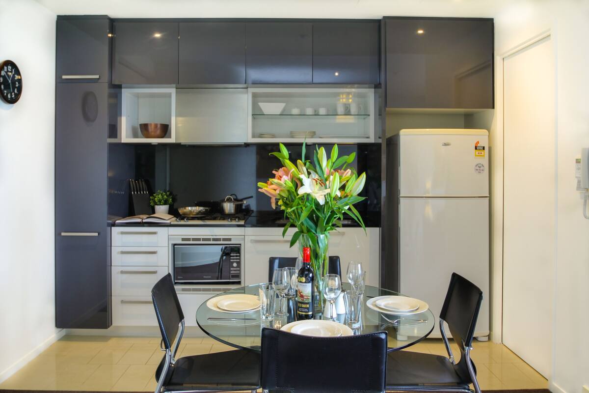 A modern kitchen with grey cabinets, a white refrigerator, and a dining table set for four.