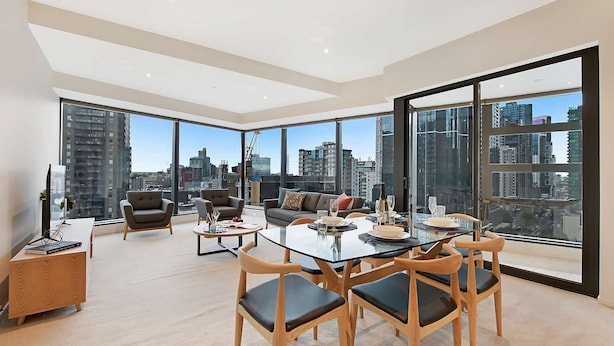 A modern dining area with a glass table, wooden chairs, and a city view through large windows. - Southbank Apartments - Eureka Tower (Southbank)