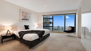 A modern bedroom with a large bed, a nightstand, a chair, and a city view through large windows. - Southbank Apartments - Eureka Tower (Southbank)