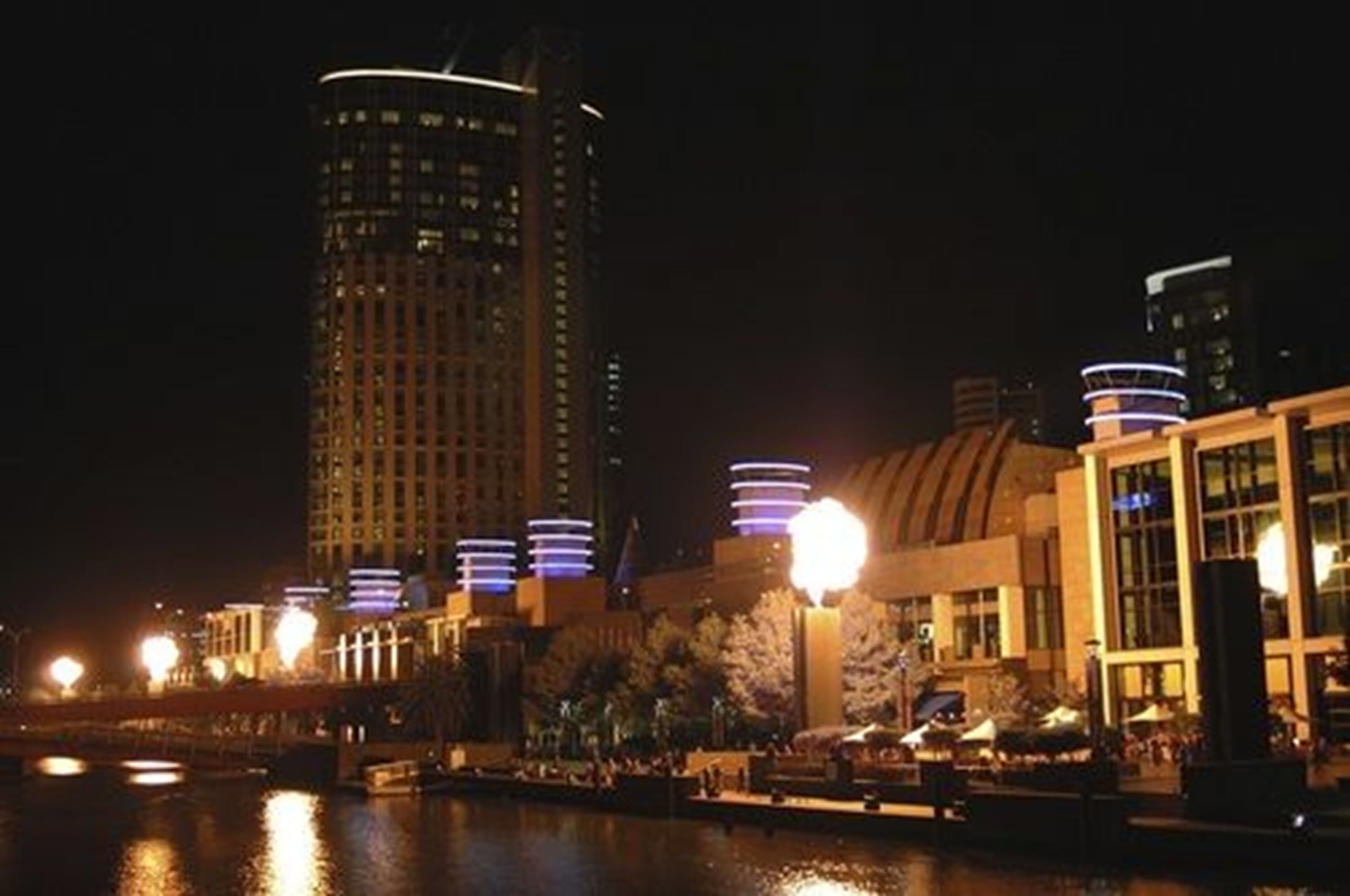 A nighttime cityscape with illuminated buildings and a waterfront.