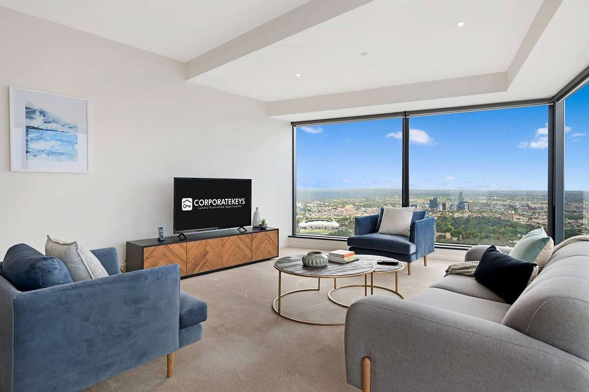 A modern living room with a large TV, comfortable seating, and a city view.