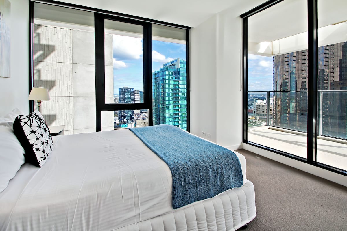 Ein modernes Schlafzimmer mit einem großen Bett und Blick auf die Stadt durch raumhohe Fenster. Eine Stadtansicht ist draußen sichtbar.