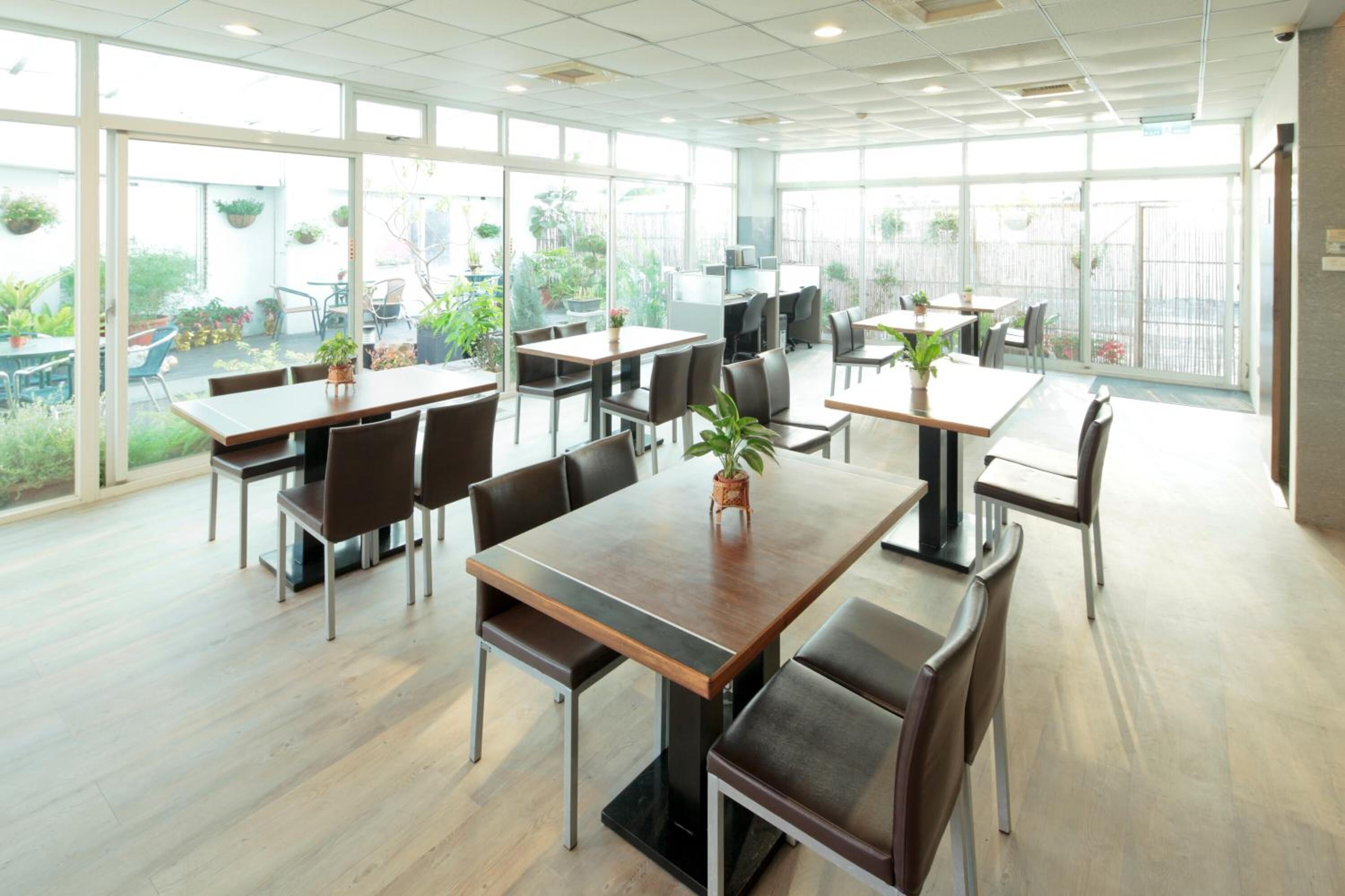 Un vaste espace de restauration intérieur, doté de nombreuses tables et chaises, de grandes fenêtres et de plantes en pot.