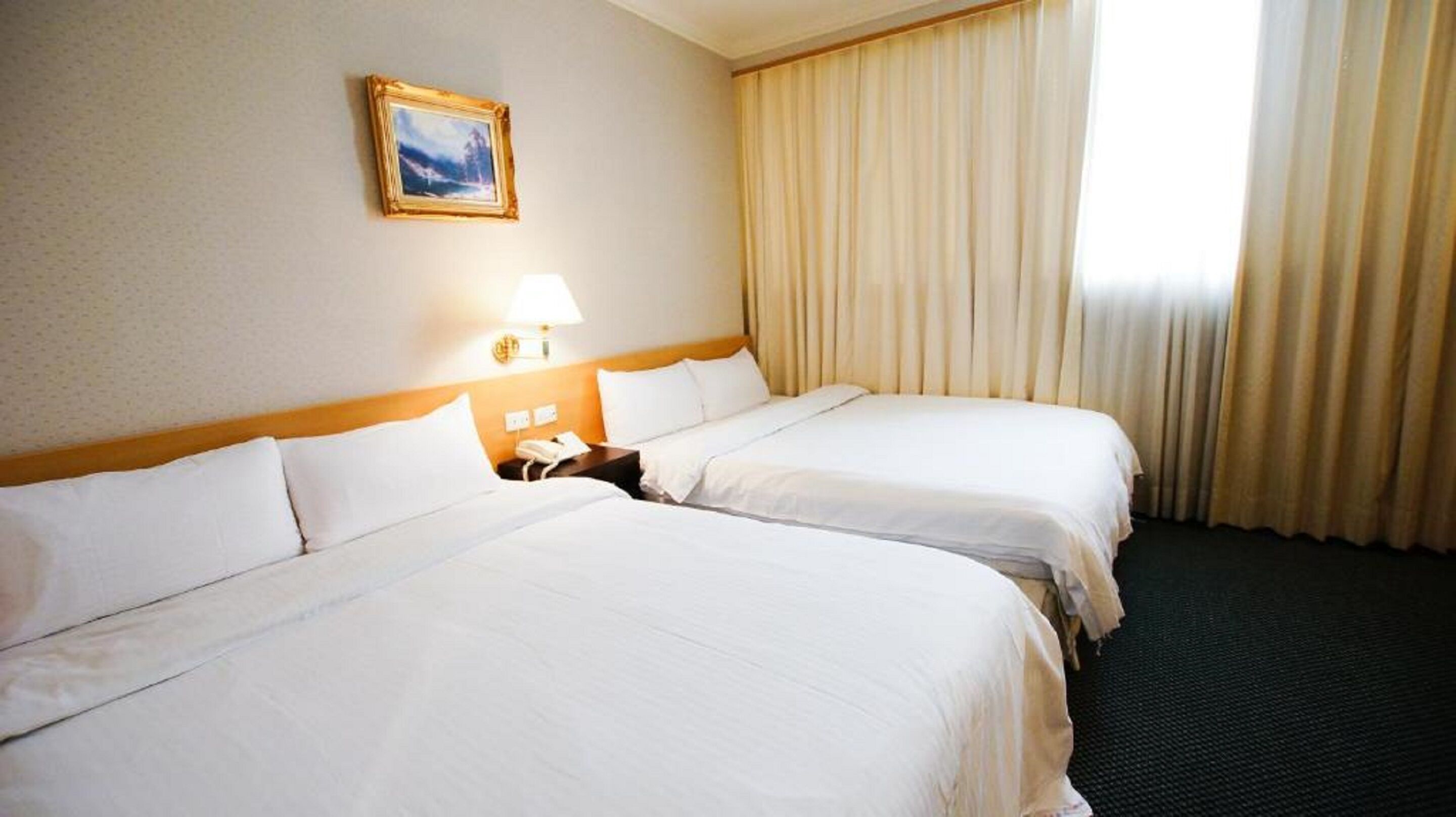 A hotel room with two beds, a nightstand, a lamp, and a painting on the wall.