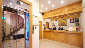 Un espace d’accueil d’hôtel avec un comptoir de réception en bois, un escalier et un panneau d’accueil encadré.