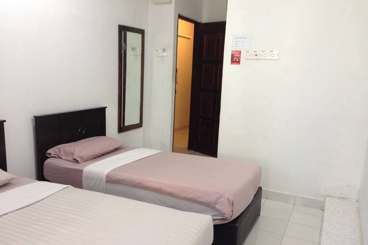 A hotel room with two single beds, a wooden headboard, a mirror, a door, and a wall-mounted light switch.