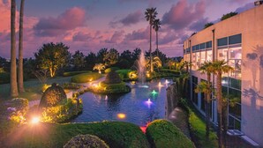 A landscaped garden with a water feature, palm trees, and a modern building with large windows. - Kensington Resort Seogwipo (Seogwipo)