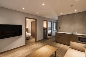 Una camera d'albergo moderna con televisore a schermo piatto, divano, tavolo da pranzo, angolo cottura e bagno.