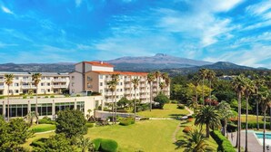 A hotel with multiple floors, a swimming pool, and a mountainous backdrop. - Kensington Resort Seogwipo (Seogwipo)