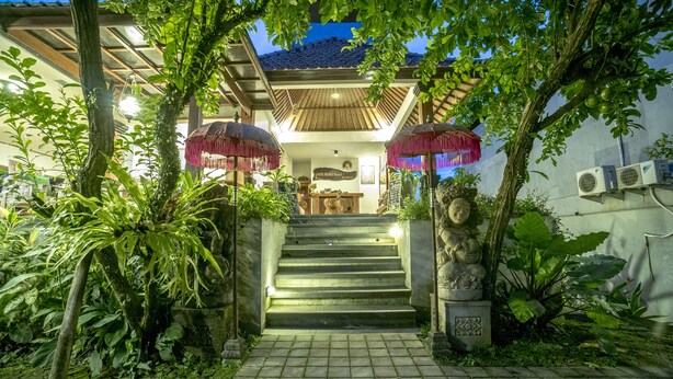 A building with a staircase leading to a covered entrance, surrounded by lush greenery and stone pillars. - Gita Maha Hotel (Ubud)