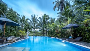 A swimming pool with lounge chairs and umbrellas, surrounded by tropical vegetation. - Gita Maha Hotel (Ubud)