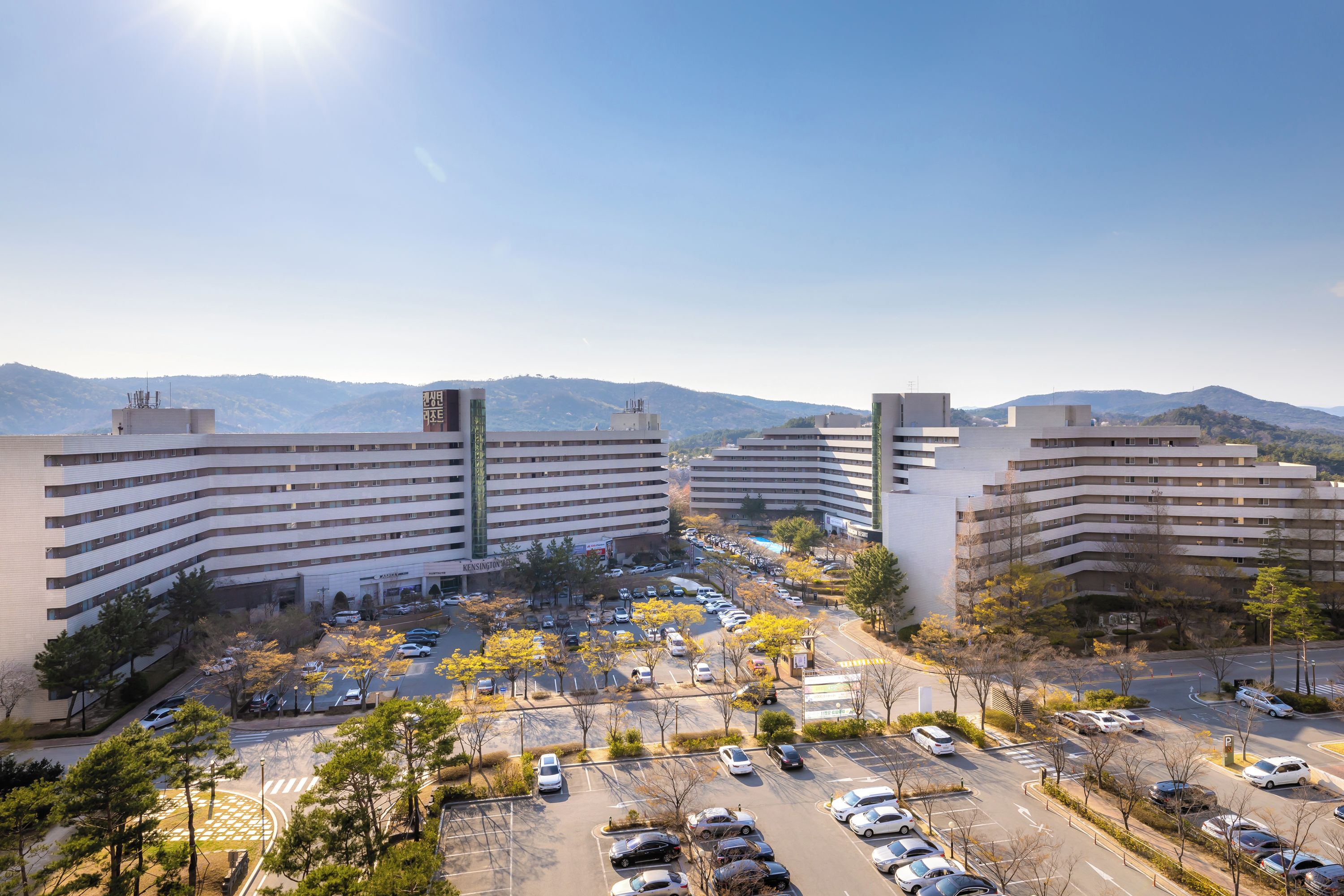 A multi-story hotel with a parking lot and surrounding trees.