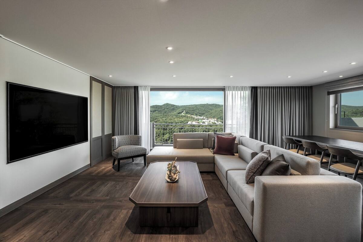 Ein modernes Wohnzimmer mit einem großen Flachbildfernseher, einer Couch, einem Couchtisch und einem Essbereich mit Tisch und Stühlen.