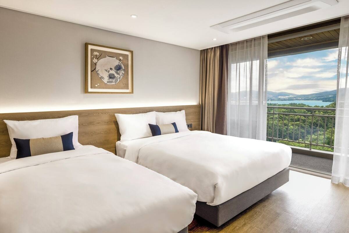 Ein Hotelzimmer mit zwei Betten, einem großen Fenster mit Blick auf eine Berglandschaft und einem gerahmten Kunstwerk an der Wand.