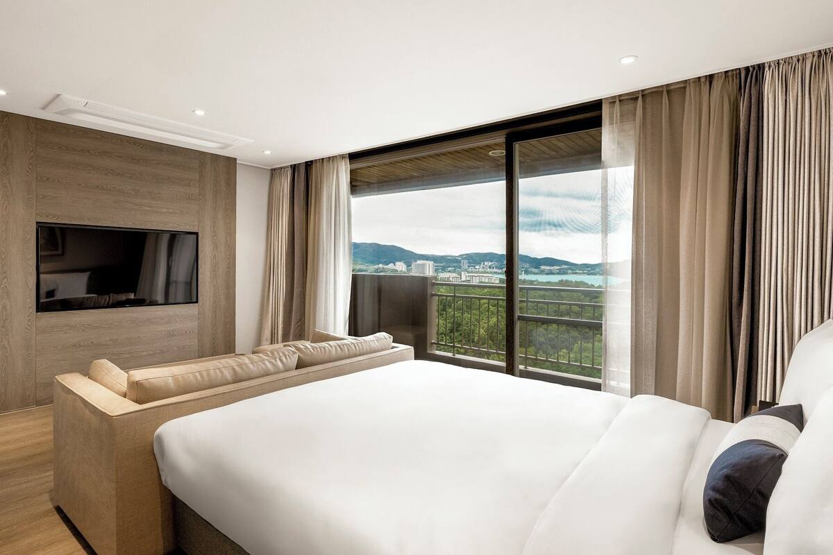Ein modernes Hotelzimmer mit einem großen Bett, einem an der Wand befestigten Flachbildfernseher und einem Balkon mit Blick auf die Stadt.
