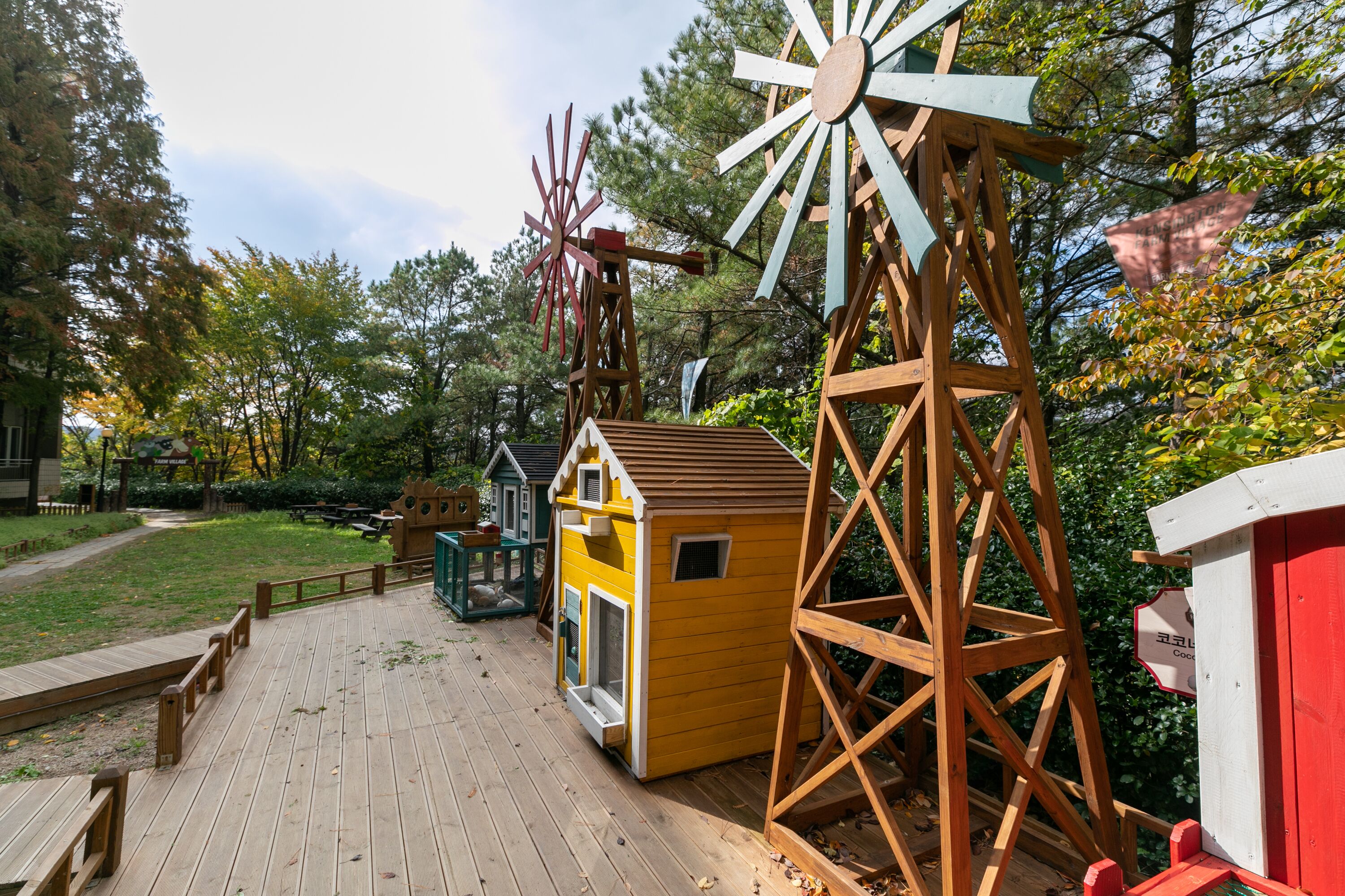A wooden deck with a yellow playhouse, a red shed, and a large windmill.