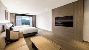Ein modernes Hotelzimmer mit einem großen Bett, einer Couch, einem an einer Holzverkleidung angebrachten Fernseher und einem Balkon mit Bergblick.