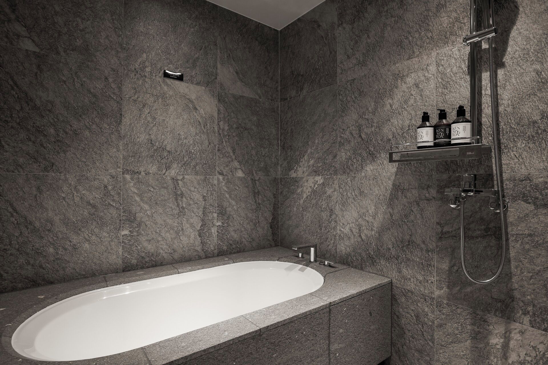 A modern bathroom with a freestanding bathtub, a shower with a handheld showerhead, and a shelf with toiletries.