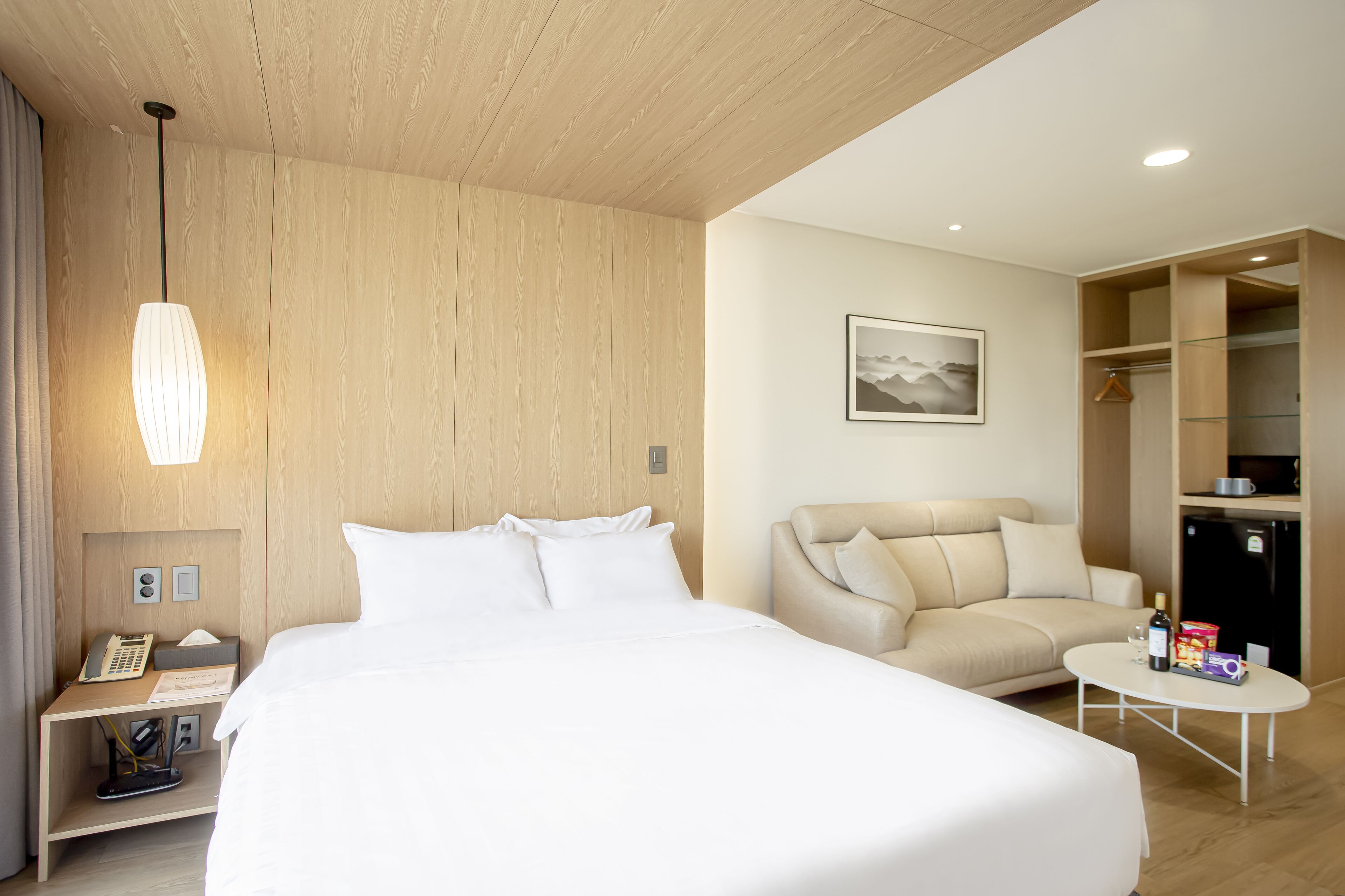 A hotel room with a large bed, a sofa, a small table, a wardrobe, and a hanging light fixture.