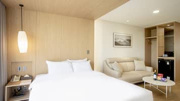 A hotel room with a large bed, a sofa, a small table, a wardrobe, and a hanging light fixture.