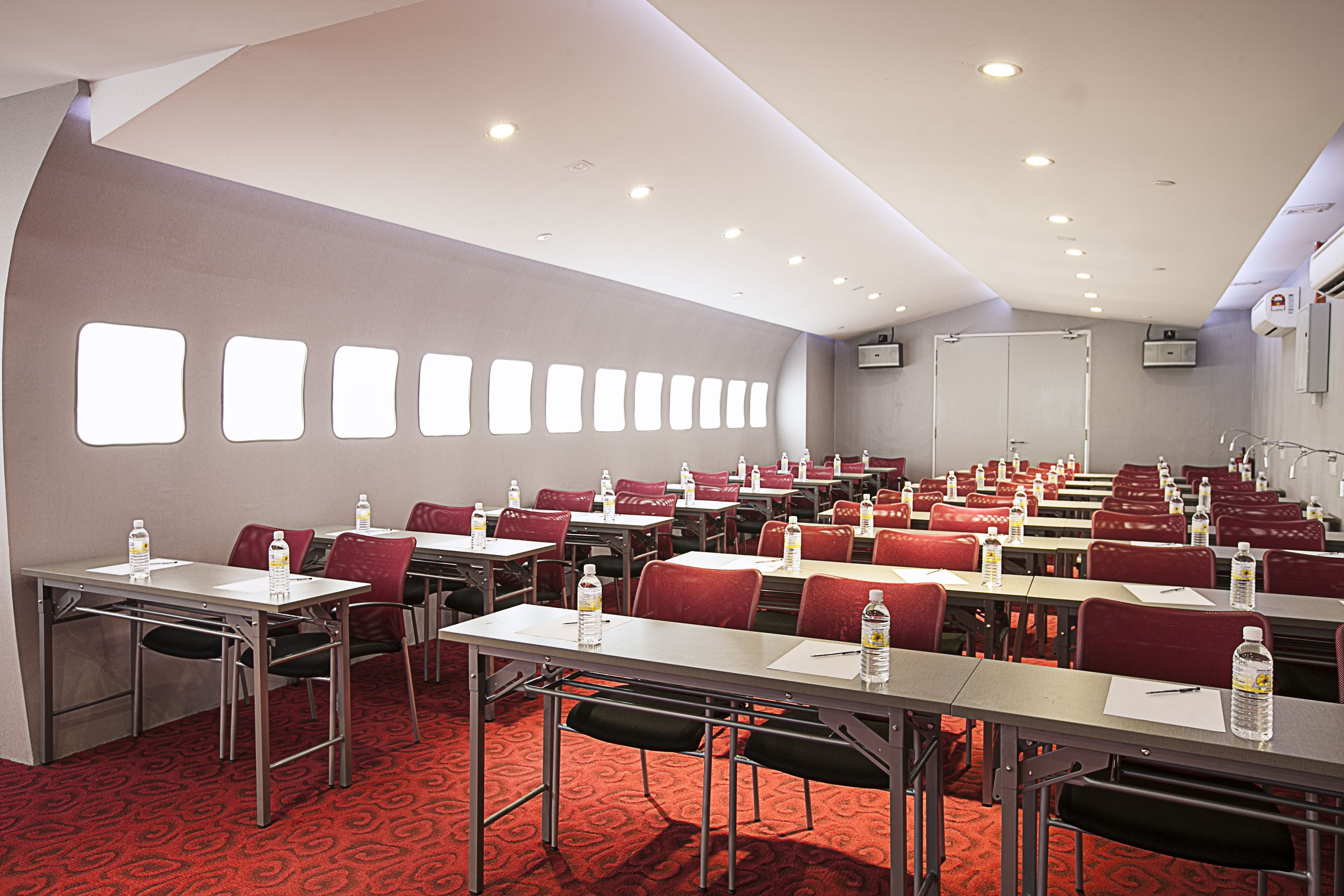 A conference room with rows of tables and chairs, equipped with water bottles and pens.