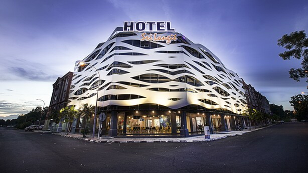 A modern hotel with a unique wavy facade, a prominent 'HOTEL' sign, and a well-lit entrance.