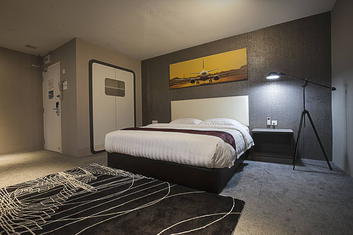 A bedroom with a bed, a nightstand, a lamp, a door, and a painting on the wall.