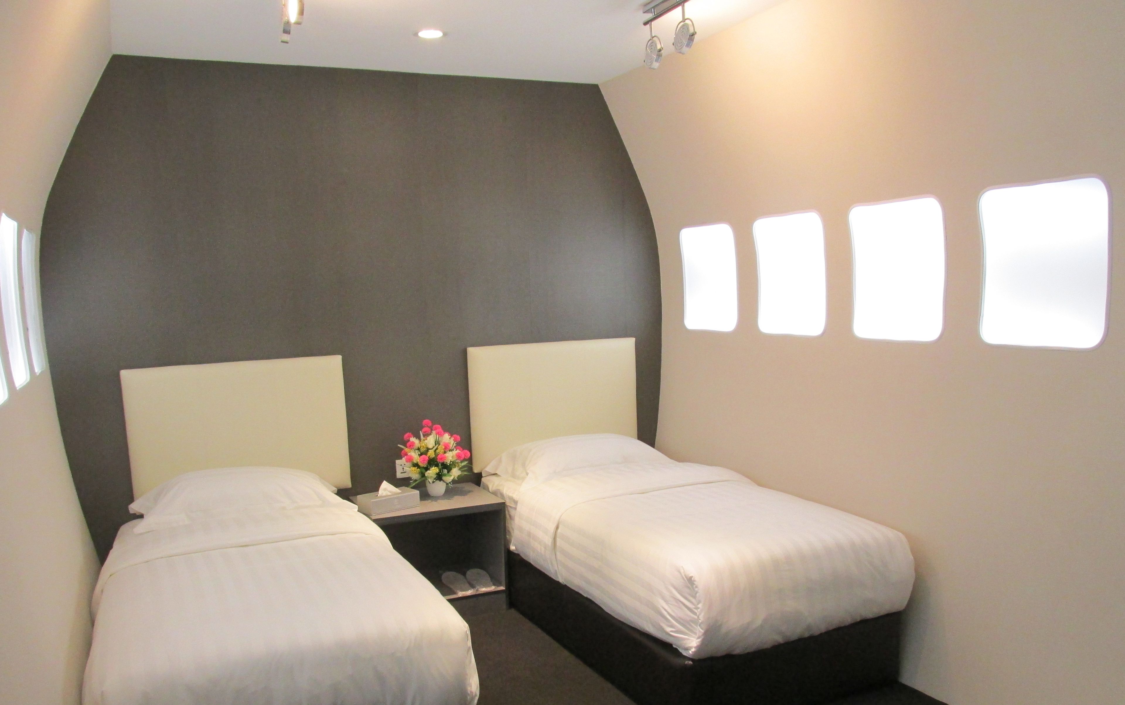 A hotel room with two single beds, a nightstand with a vase of flowers, and a large window with multiple panes.