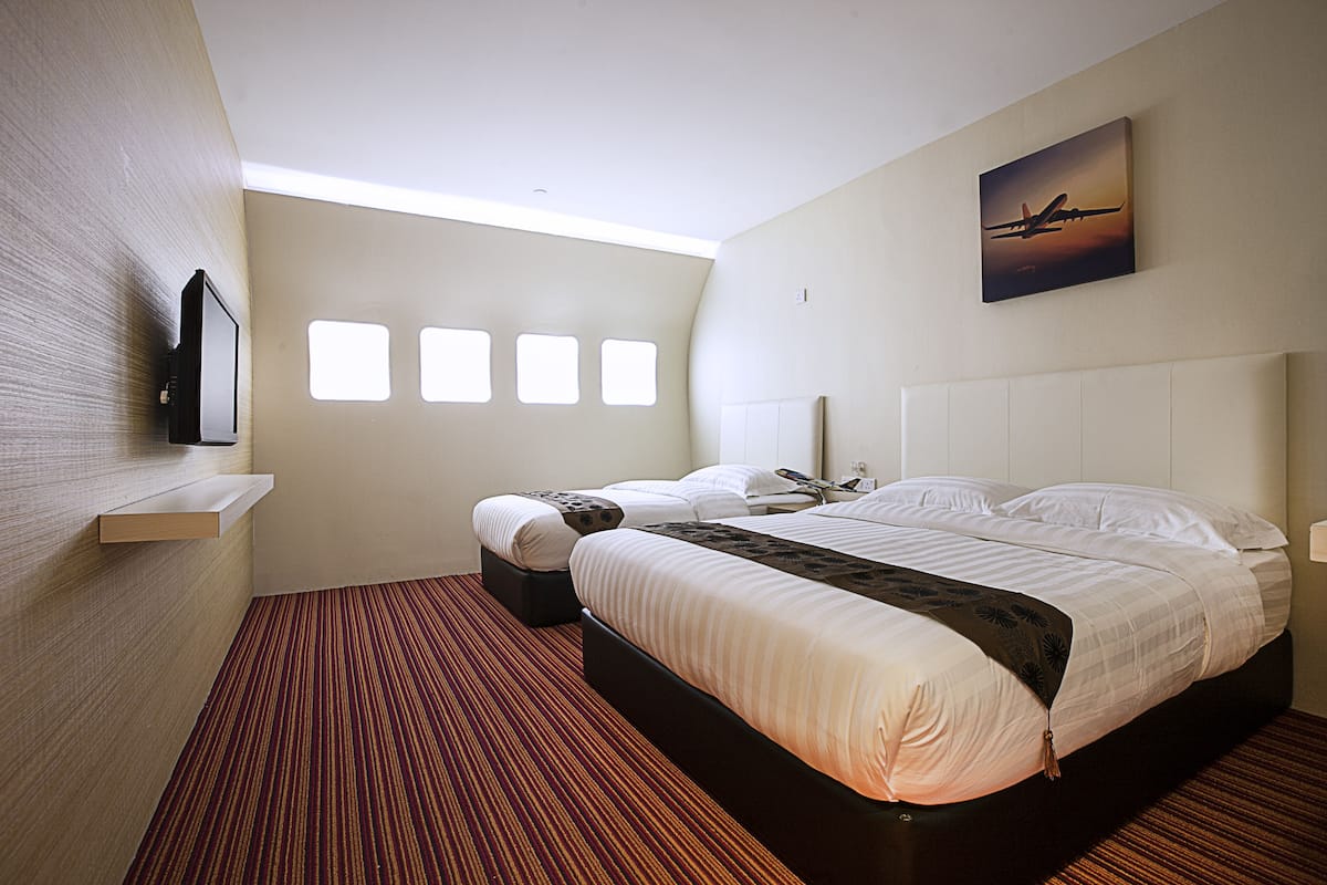 A hotel room with a large bed, a TV mounted on the wall, and a painting of an airplane.