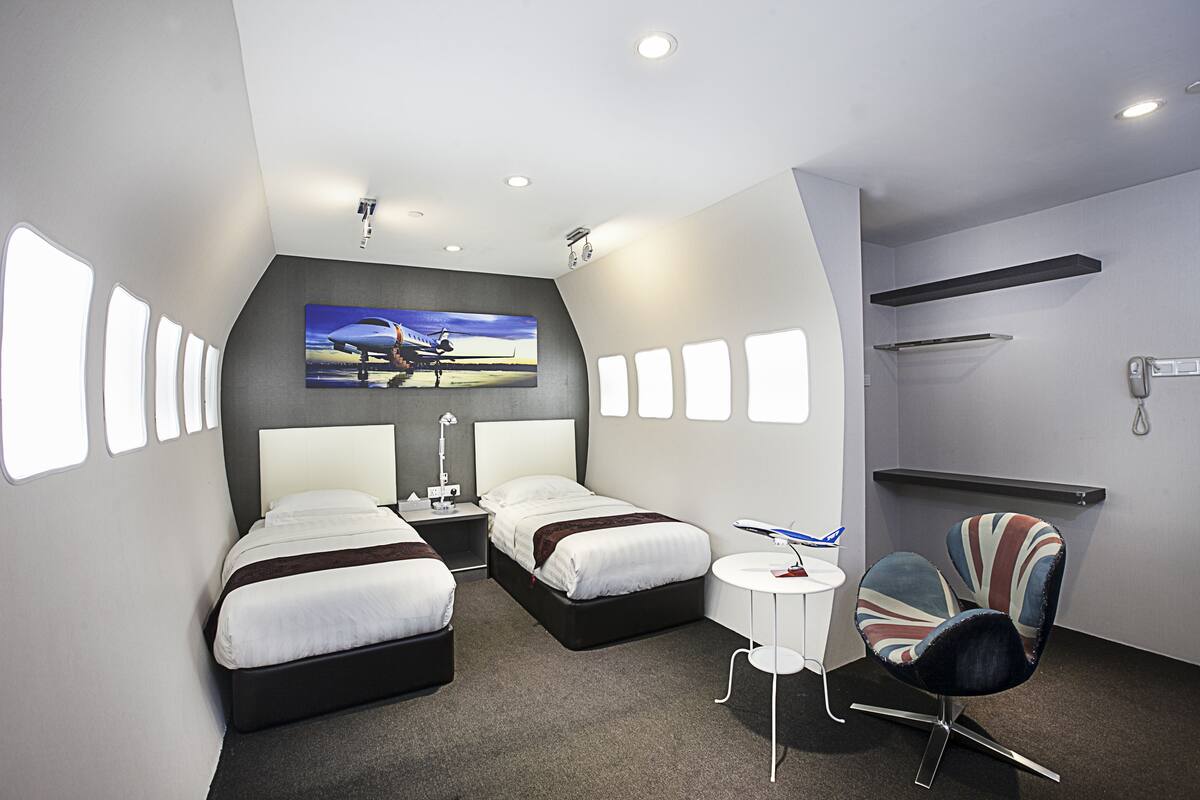A modern hotel room with two beds, a small table, a chair, and a large window.