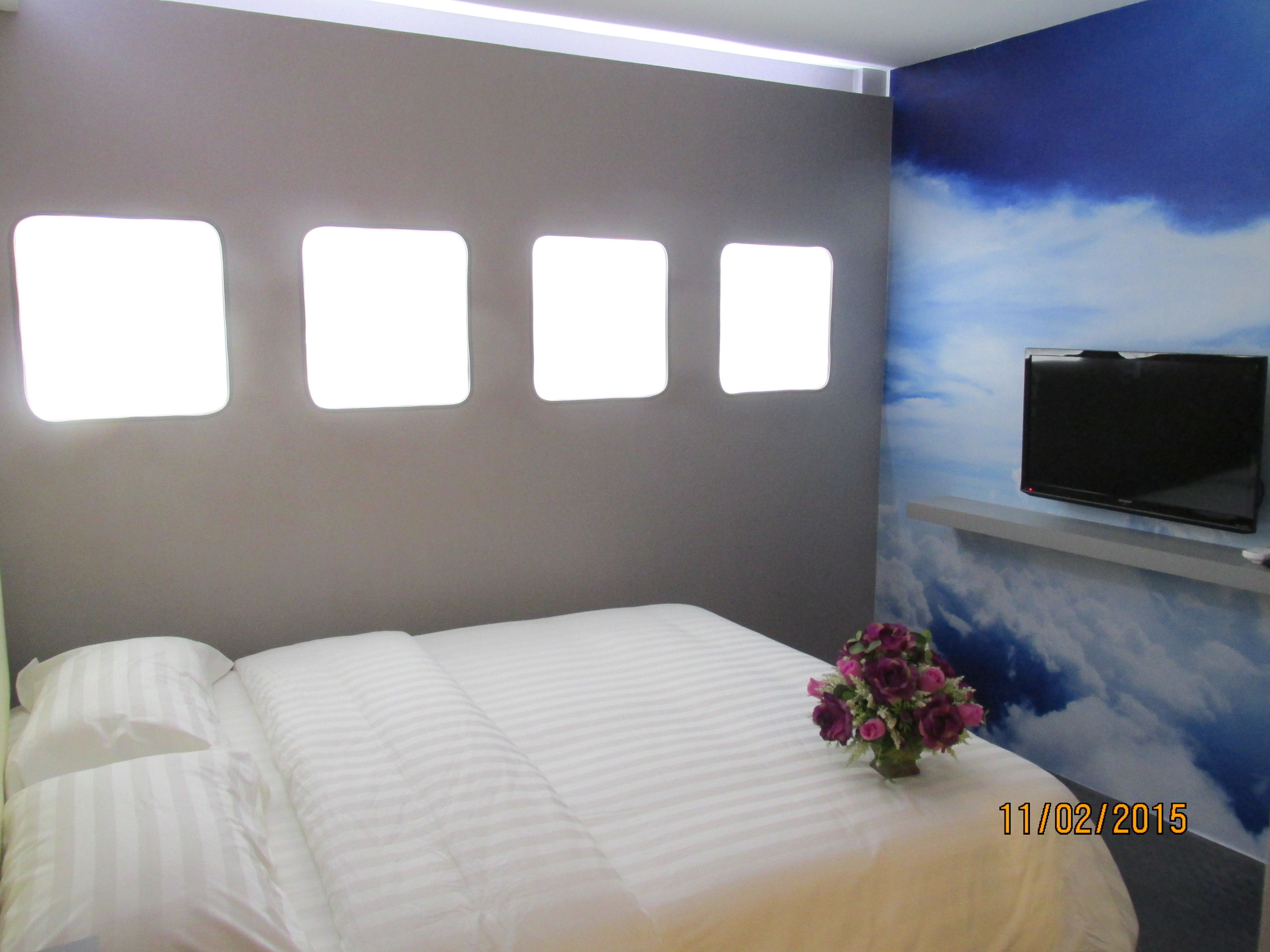 Habitación de hotel con una cama, un televisor montado en la pared y un diseño decorativo de nubes en la pared.