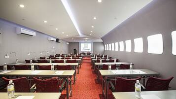A conference room with rows of tables and chairs, a red carpet, and a projector screen at the front.