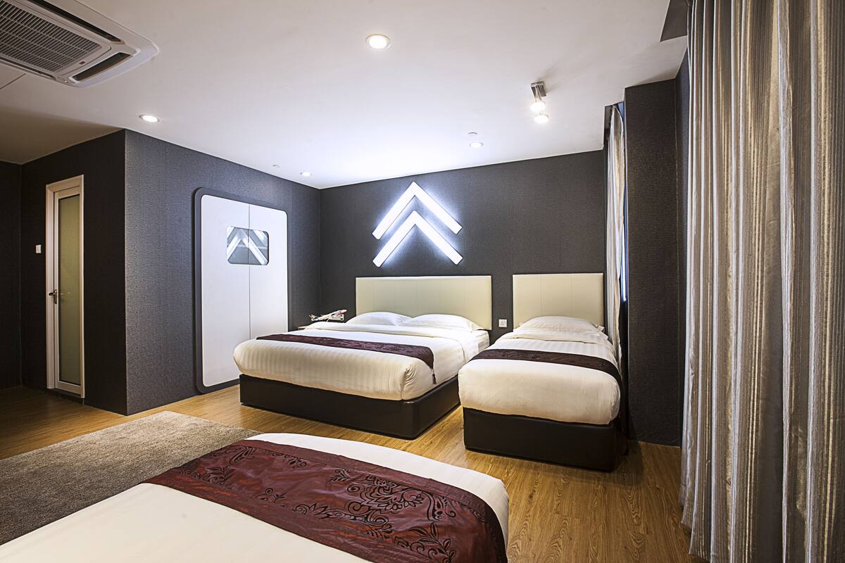 A modern hotel room with two beds, a large mirror, and a distinctive arrow-shaped light fixture on the wall.