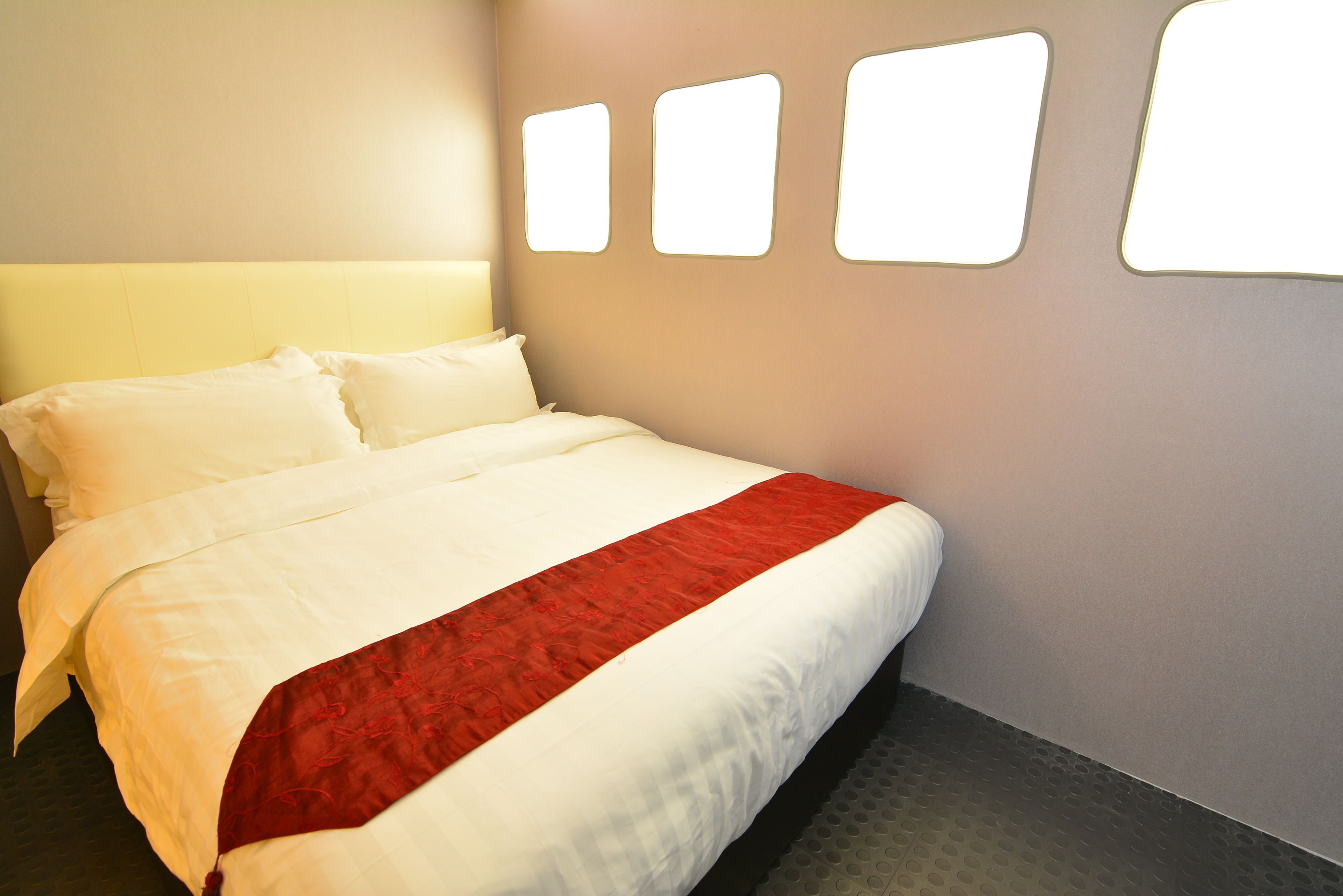 Una cama bien hecha con ropa de cama blanca y roja, un cabecero y una pared con tres lámparas rectangulares.