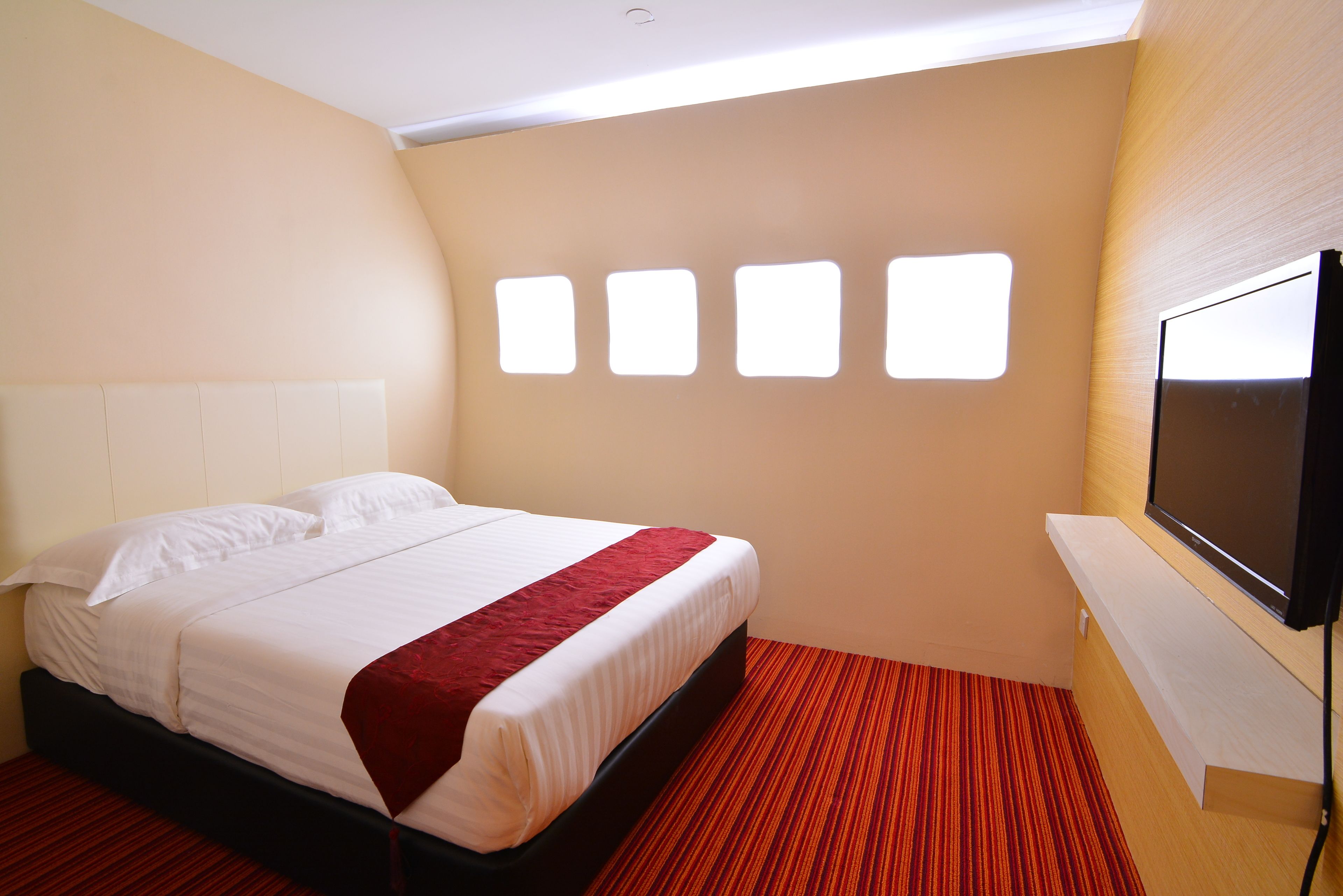 A hotel room with a bed, a TV, and a window with four square panes.