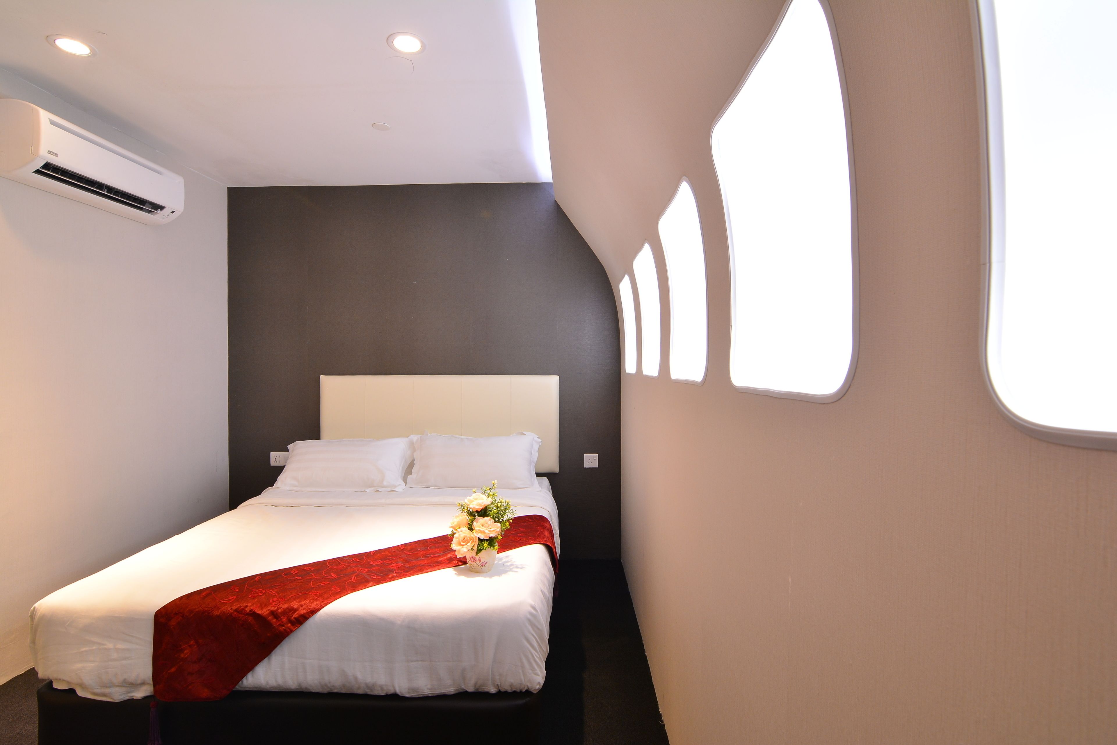 A hotel room with a bed, a red throw, and a vase of flowers.