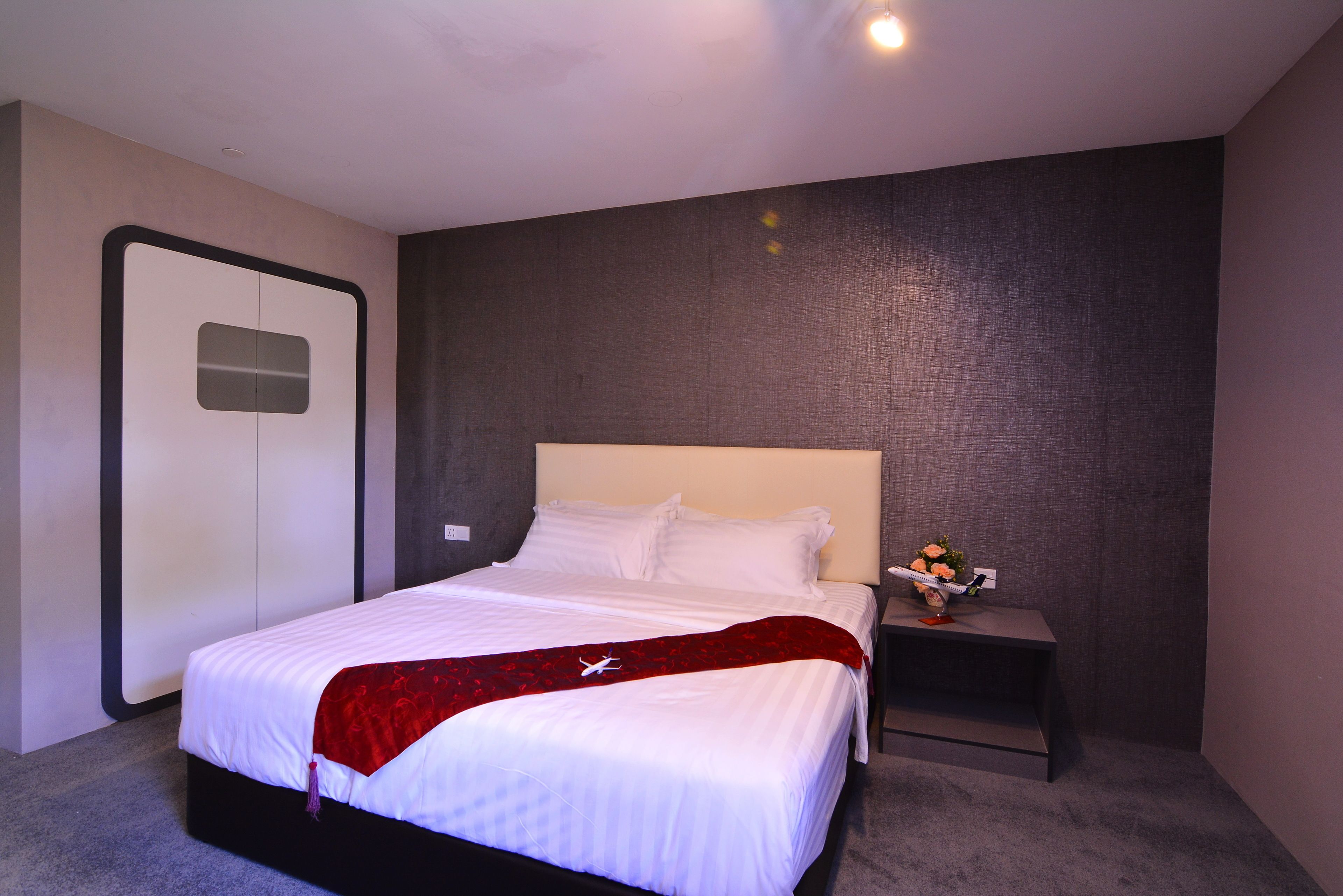 A modern hotel room with a large bed, a nightstand with a vase of flowers, and a dark textured wall.