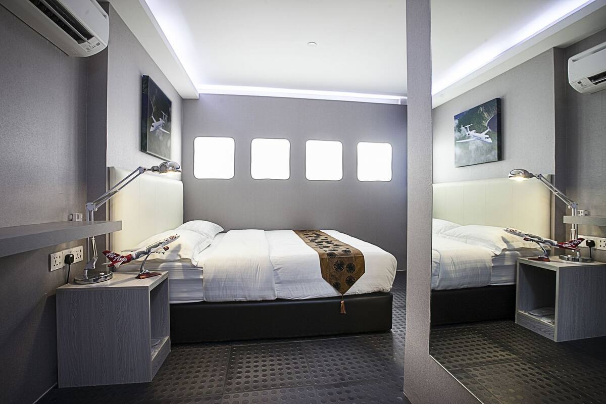 A modern hotel room with a large bed, two bedside tables with lamps, a wall-mounted air conditioner, and a window with a view.