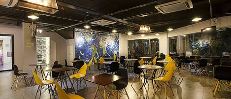 A modern dining area with tables and chairs, a large world map mural, and industrial-style lighting.