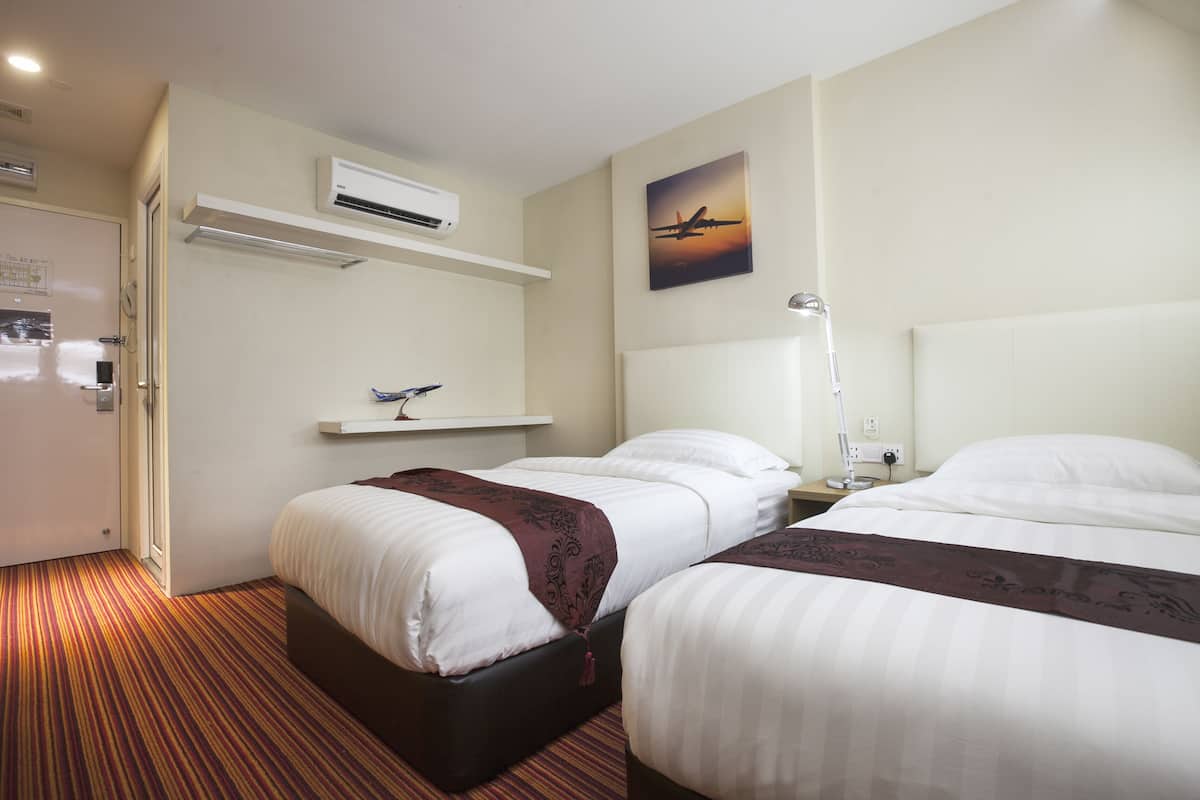 A hotel room with two beds, an air conditioner, a painting of an airplane, and a bedside lamp.