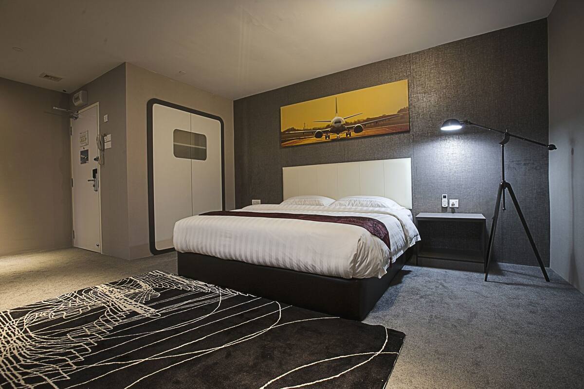 A bedroom with a bed, bedside table, lamp, and a painting on the wall.