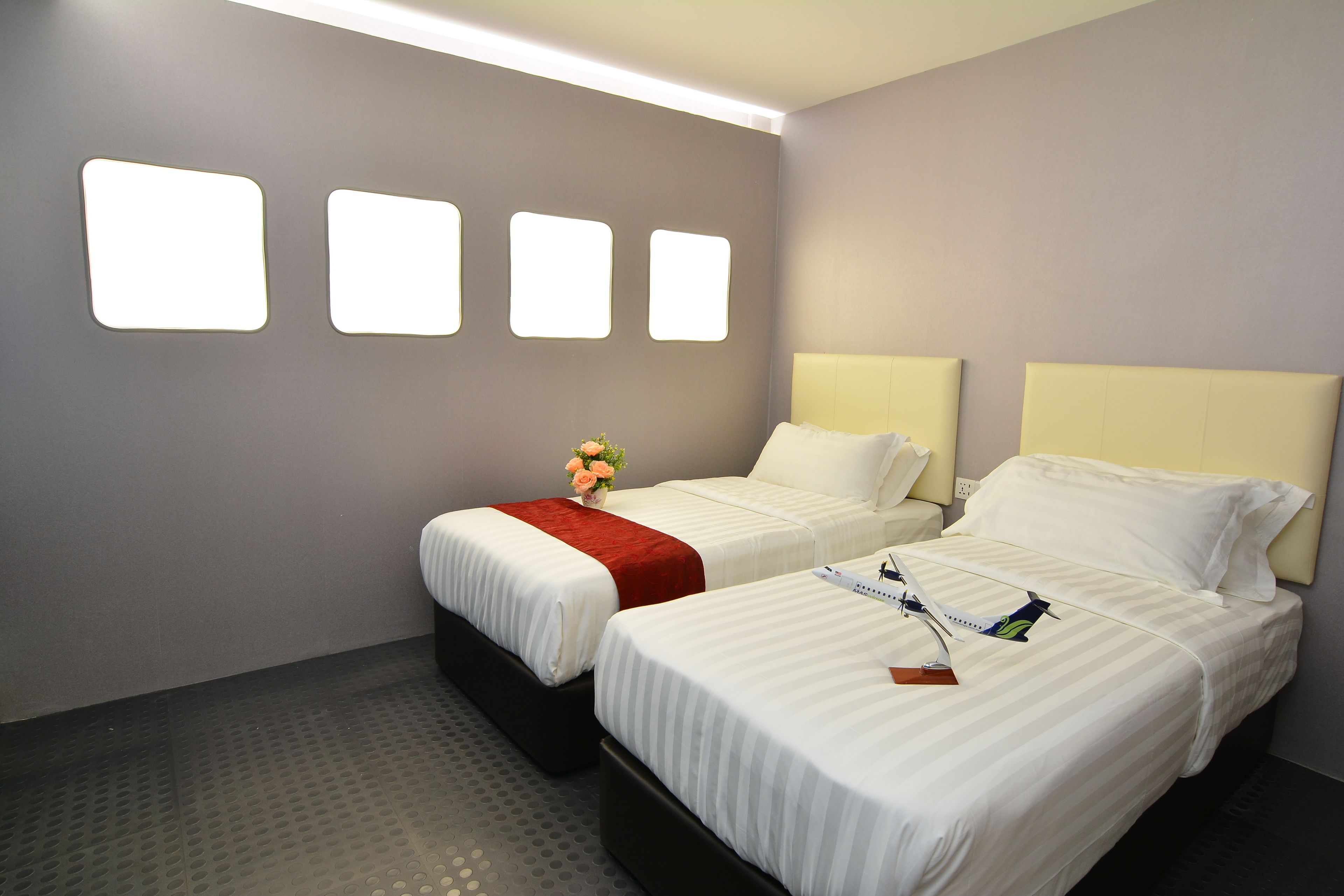 Ein Hotelzimmer mit zwei Betten, einer roten Tagesdecke und einem kleinen Tisch mit einem Blumenstrauß.