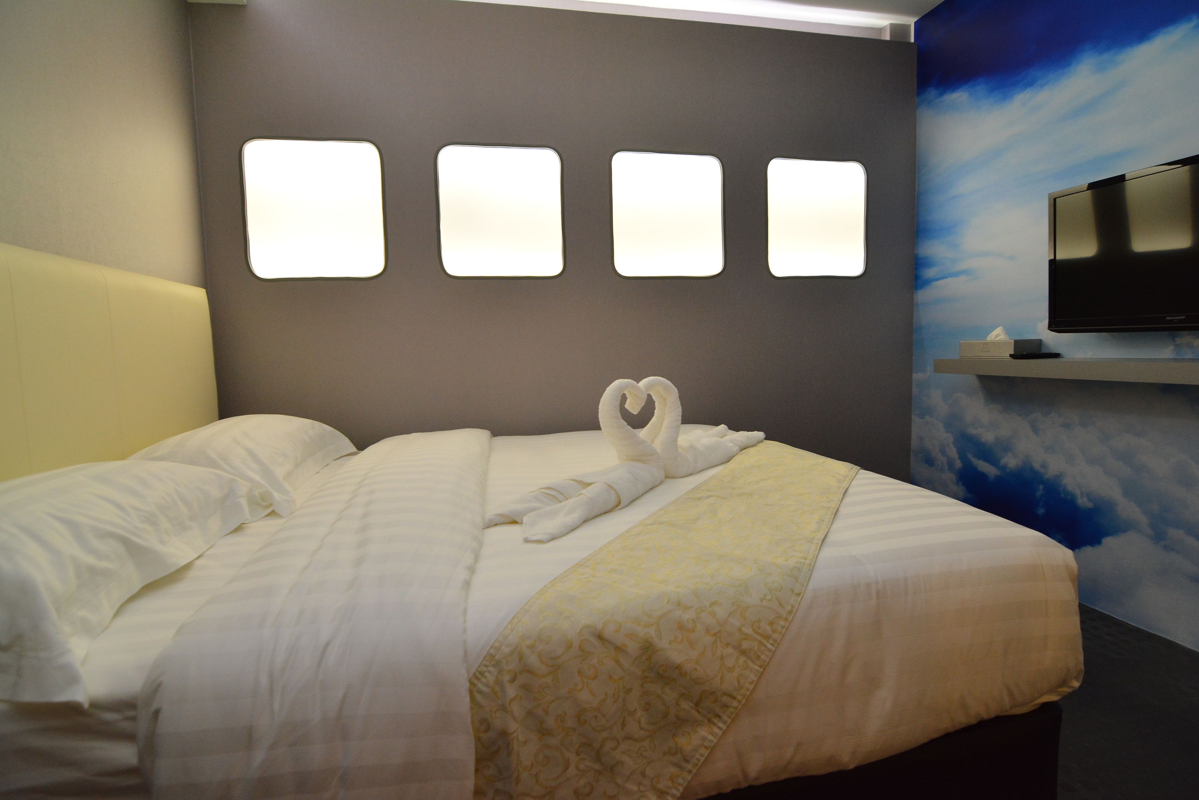Una camera d'albergo con un letto rifatto, una TV a parete e un'ampia finestra con vista sul cielo.