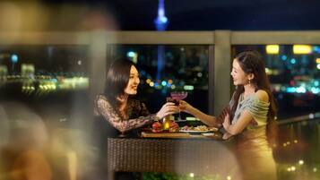 Two people sitting at a table with drinks and burgers, overlooking a cityscape with a tower in the background.