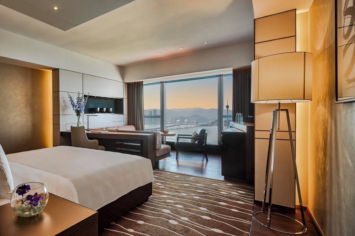 Une chambre d’hôtel moderne dotée d’un grand lit, d’un bureau et offrant une vue sur le paysage urbain.