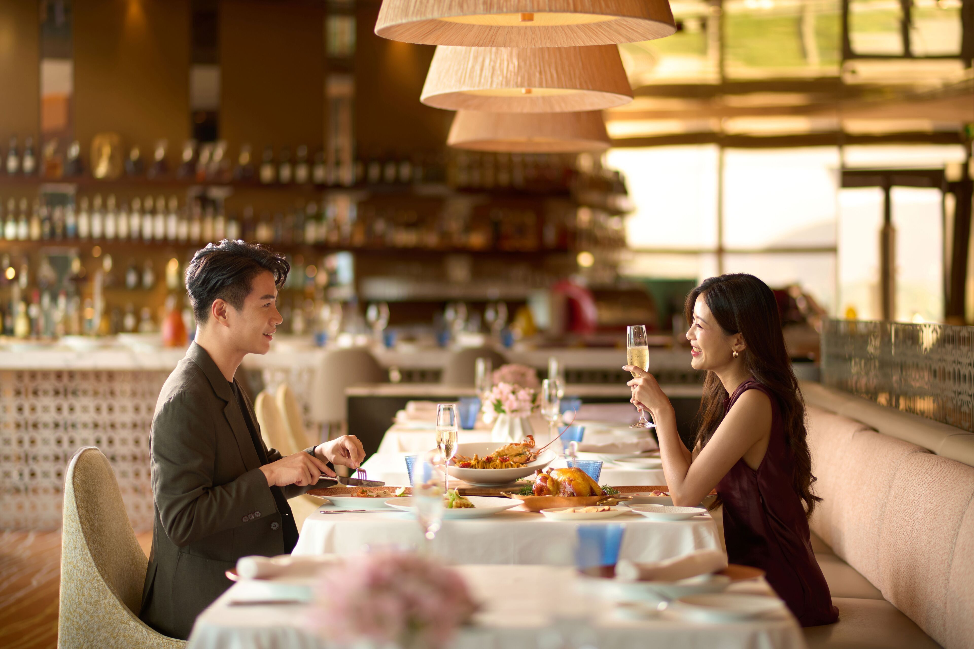 Una pareja cenando en un restaurante, con una barra de bar al fondo.