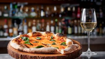 A pizza on a wooden board with a glass of white wine beside it.