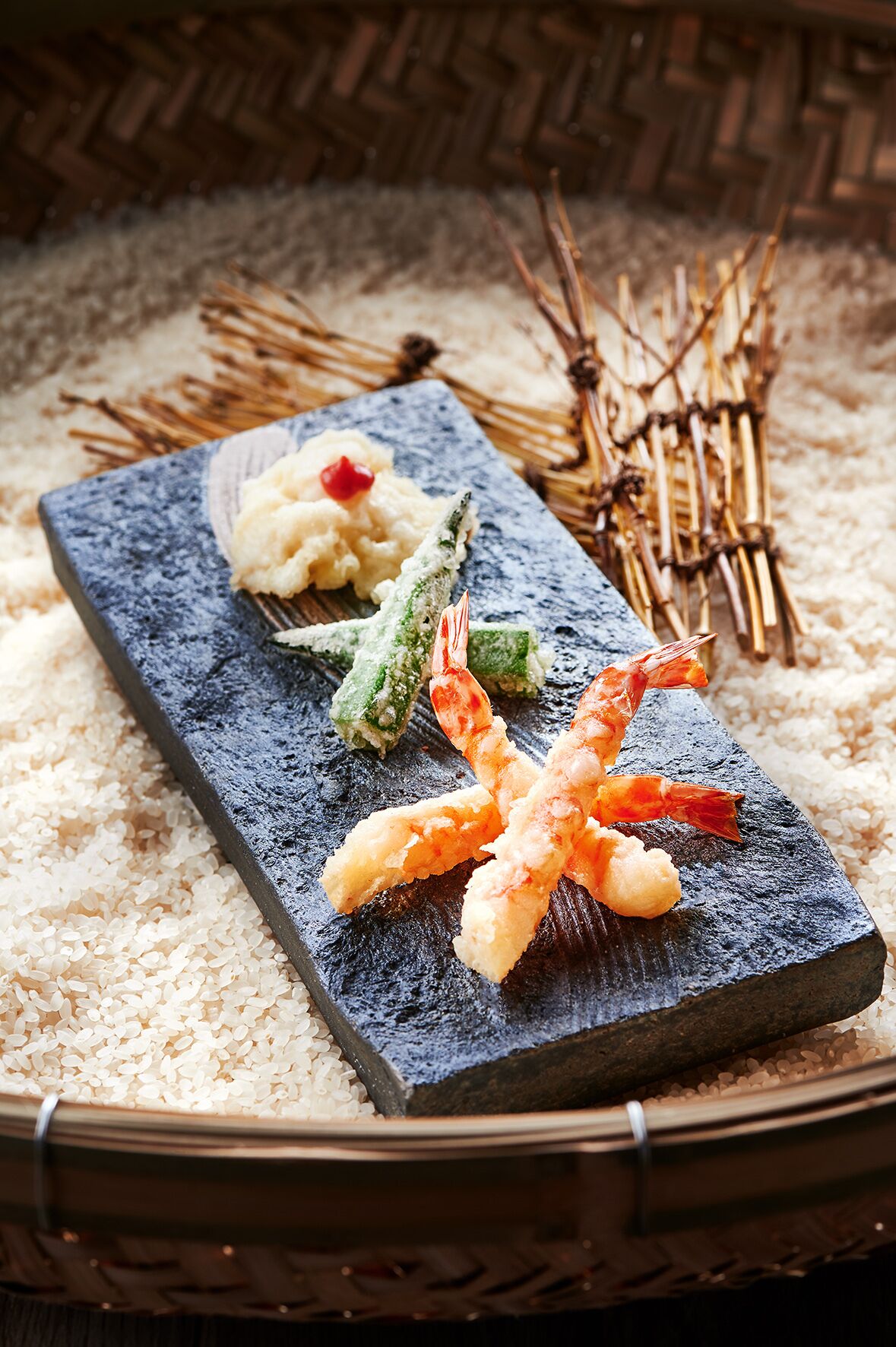 Una bandeja de sushi con camarones, verduras y arroz sobre una tabla de pizarra.