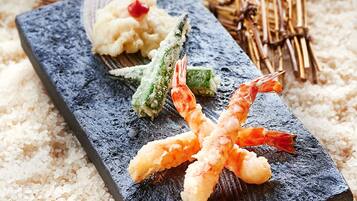 Una bandeja de sushi con camarones, verduras y arroz sobre una tabla de pizarra.